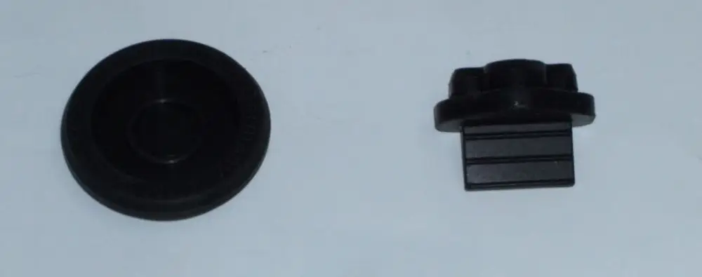 Zwei schwarze Kunststoffteile, ein runder flacher Diskus und ein rechteckiger Block mit vier Rillen, möglicherweise Teil eines Reparatursets von Daikin.